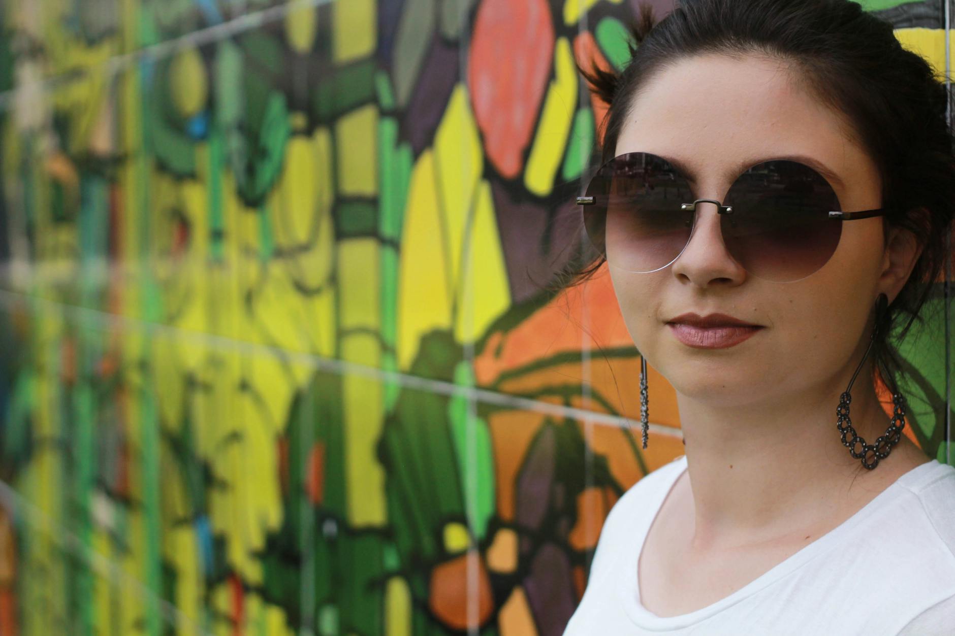 Kobieta w modnych okularach przeciwsłonecznych na tle kolorowego graffiti