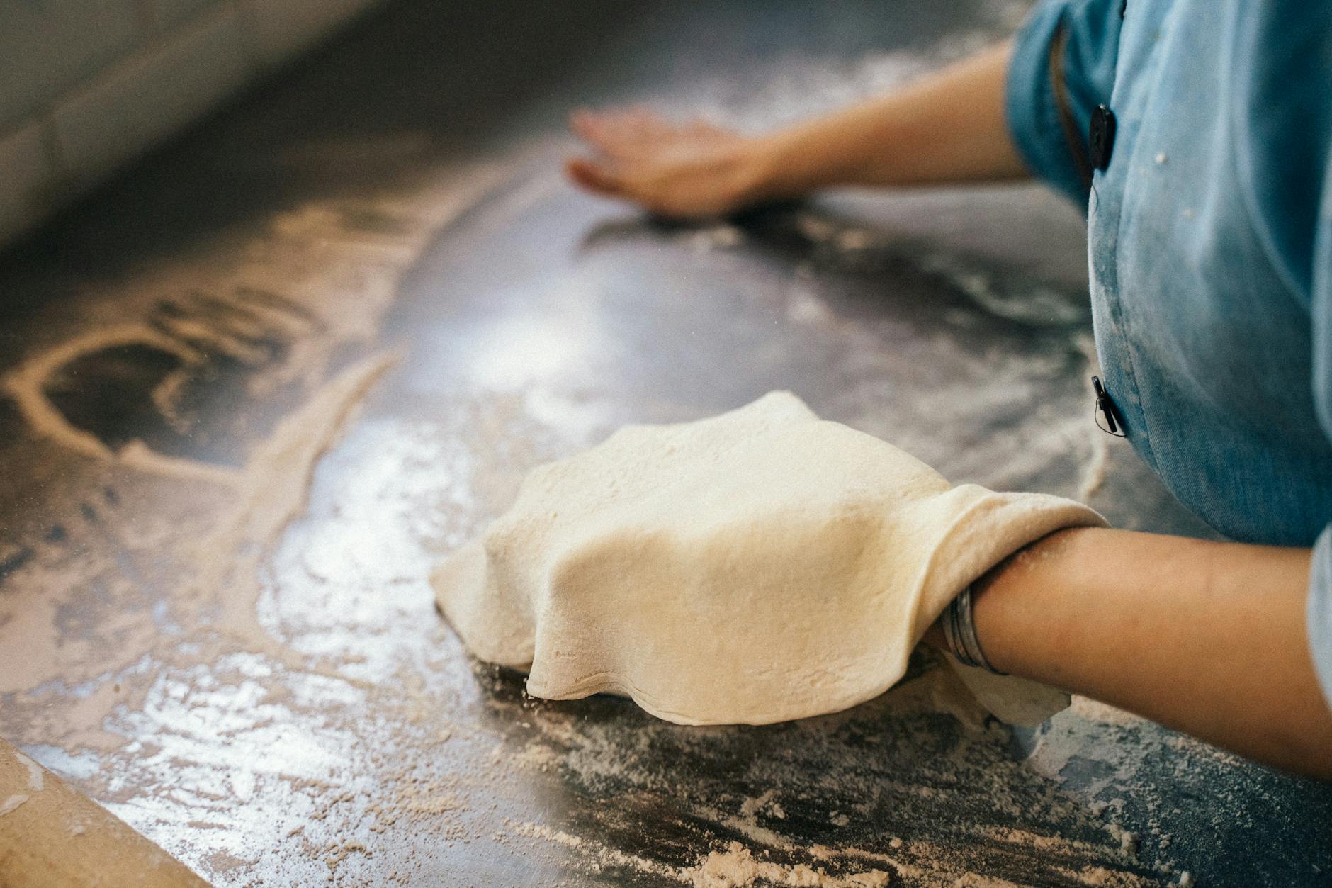 Pizzerman w niebieskiej koszuli wyrabia ciasto na posypanym mąką blacie