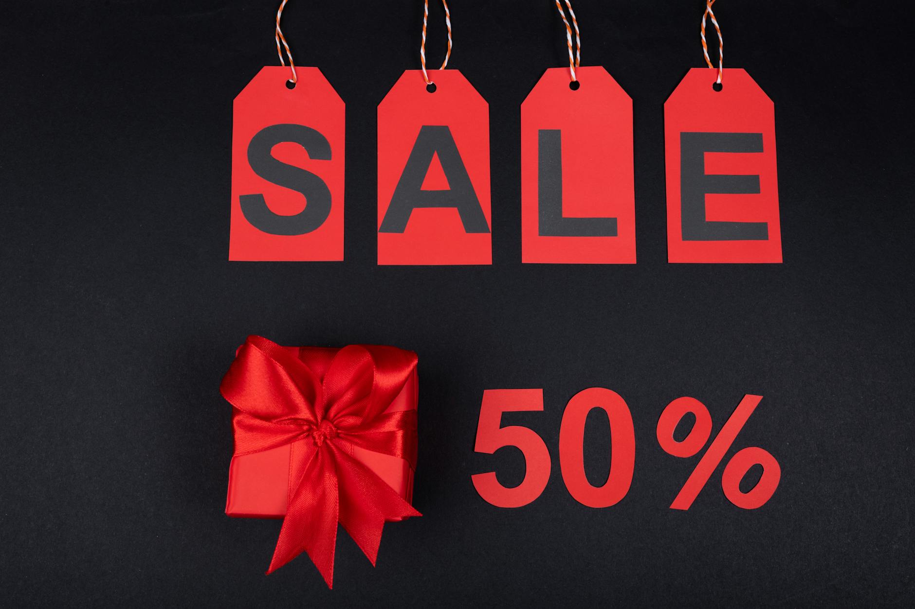 Czerwone pudełko prezentowe obok metek wyprzedaży i napisu 50% na czarnym tle