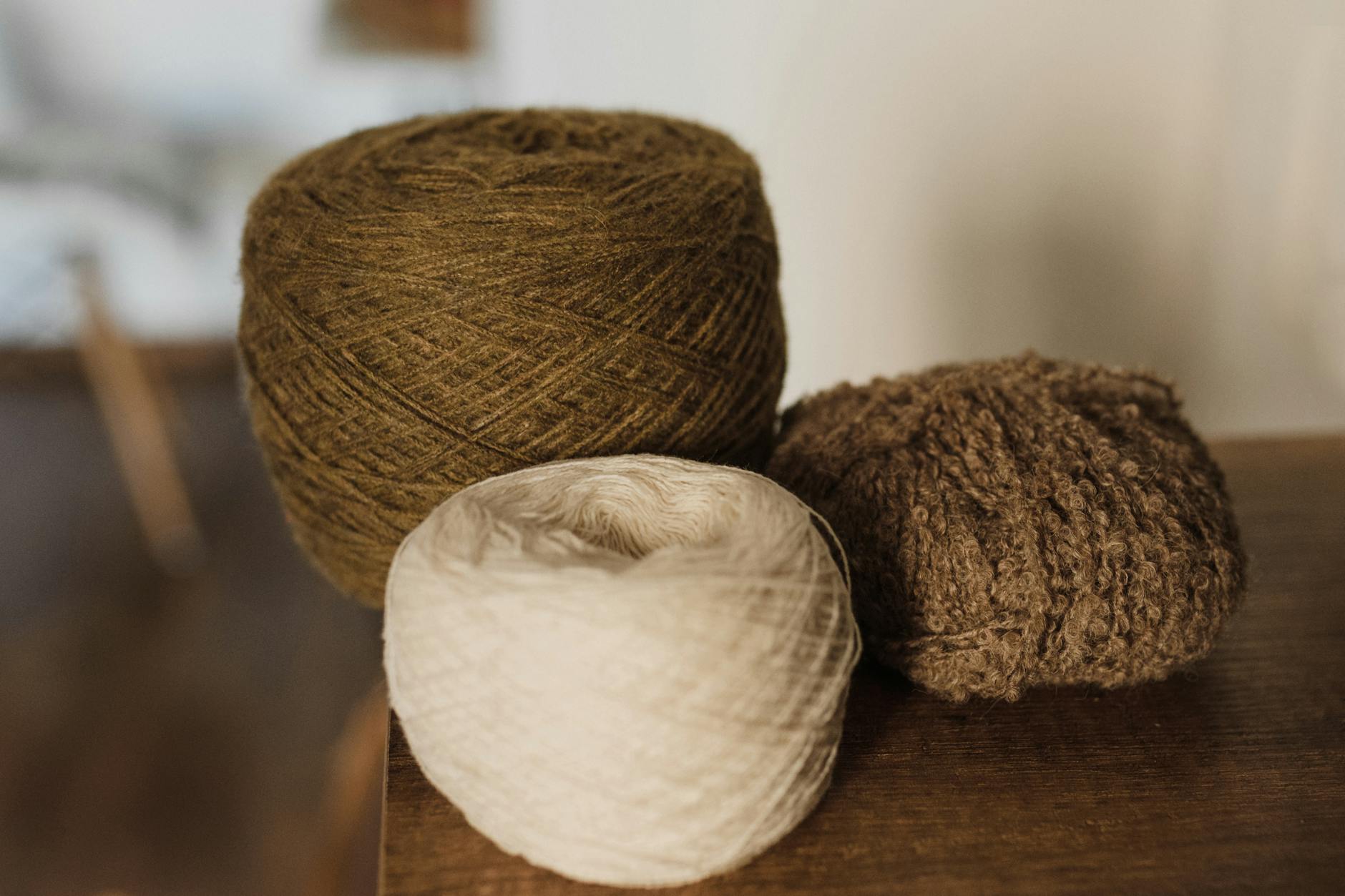 Kłęby brązowej, beżowej i kremowej włóczki ułożone na stole