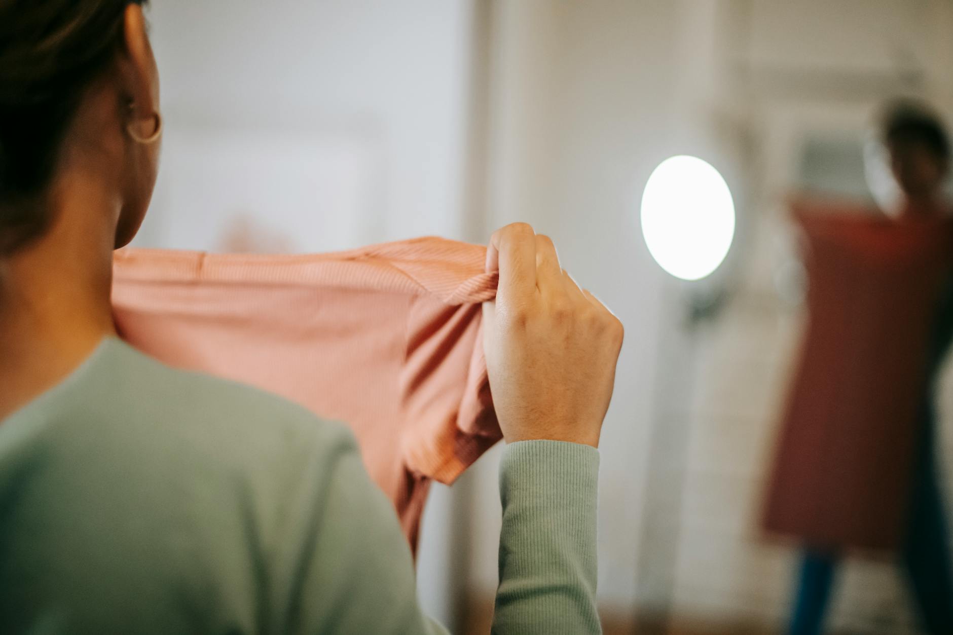 Kobieta przymierza ubrania przed lustrem w jasnym pokoju