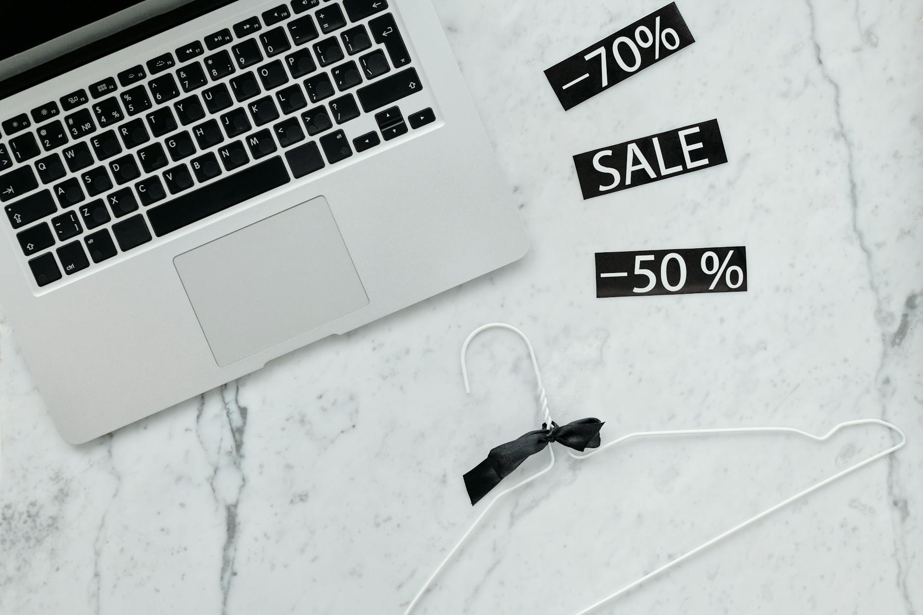 Laptop, wieszak i naklejki z napisem sale na marmurowym biurku