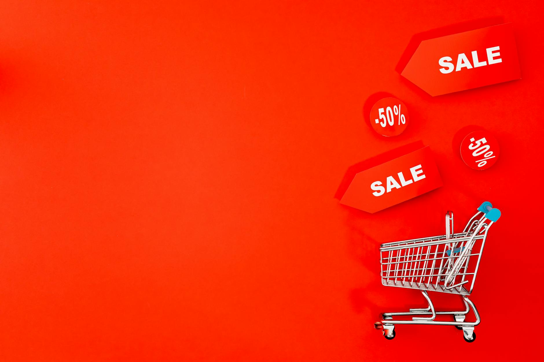 Wózek sklepowy z metkami sale na czerwonym tle promującym rabaty