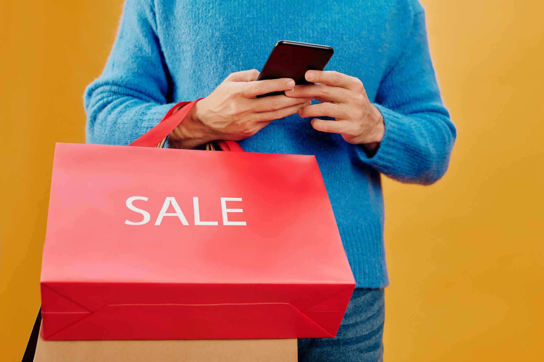 Mężczyzna trzyma torbę z napisem sale i smartfon podczas zakupów